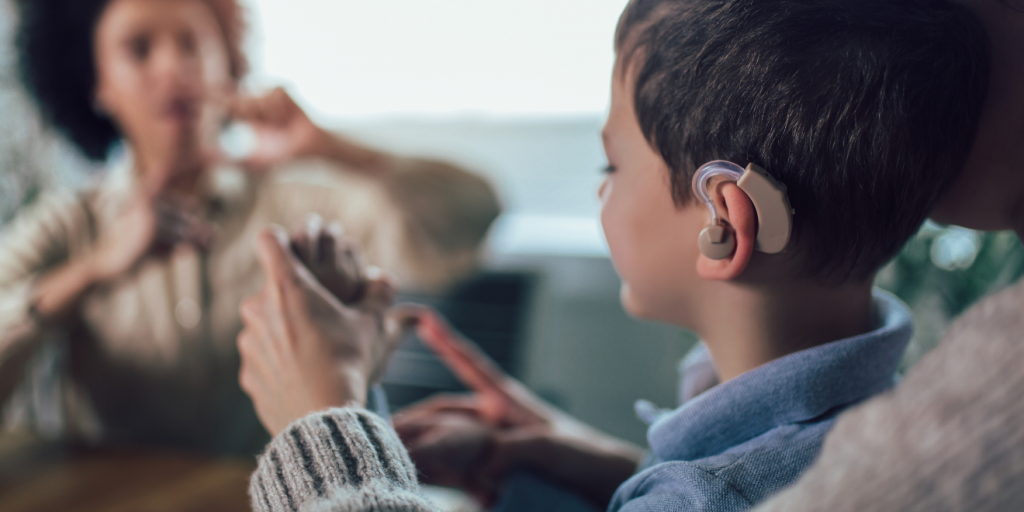 young boy with a hearing aid learning American Sign Language