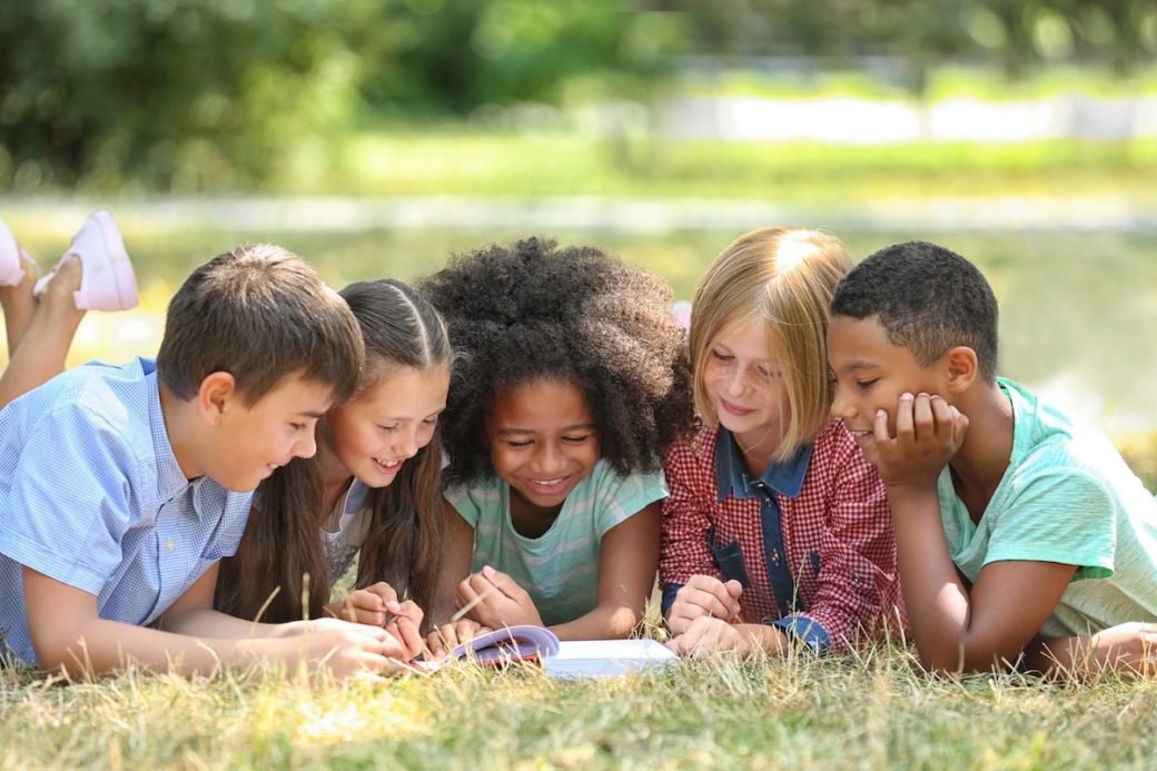 5 ids reading a book outside on grass
