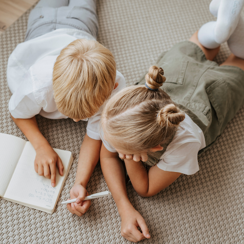 Two children looking at a journal together with a pencil